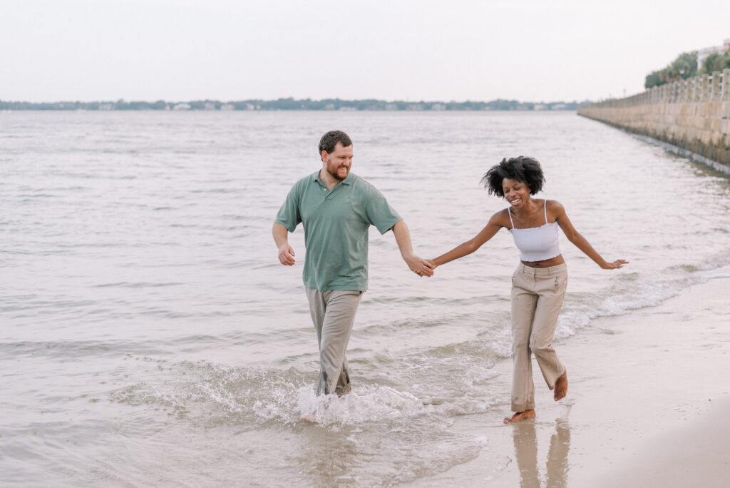 couple laugh walking on the beach in the water holding hands