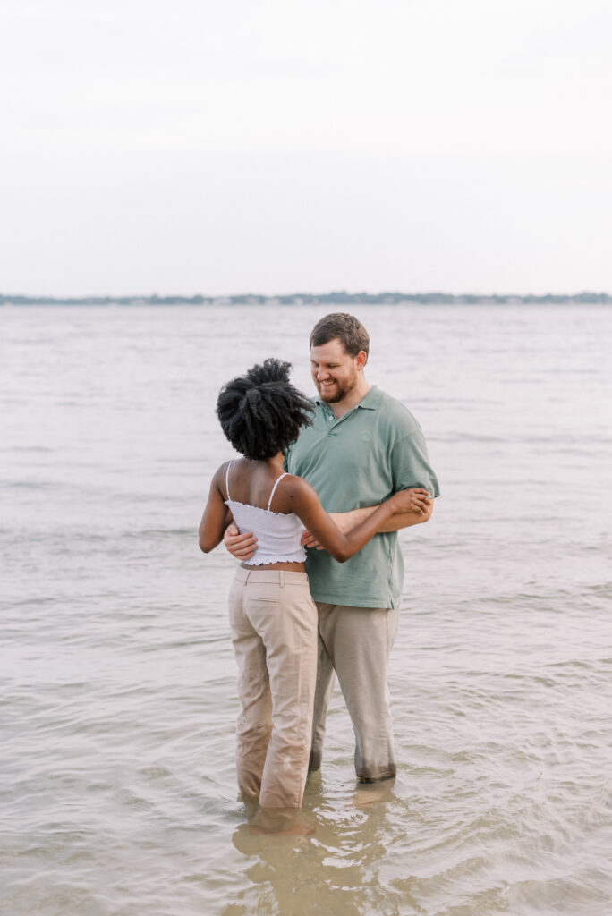 couple stand ankle deep in the ocean holding each other