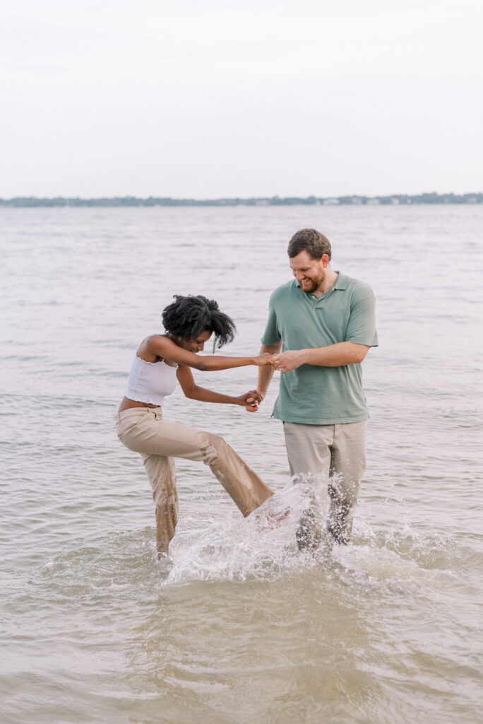 couple hold hands and stand in the water kicking water at each other