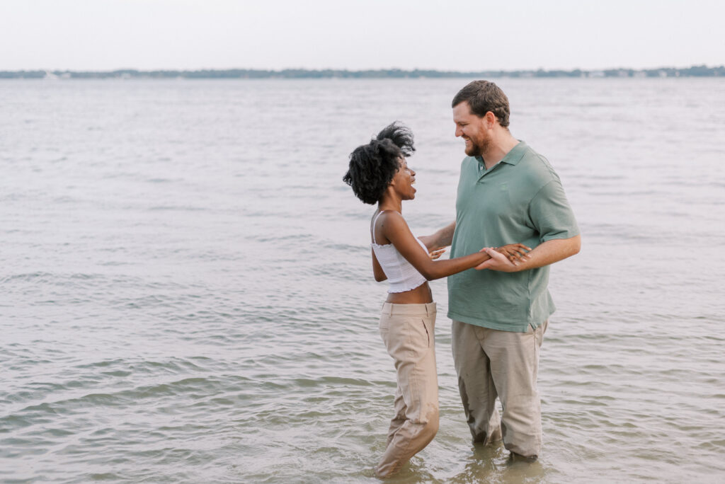 Couple holding hands and standing knee deep in the ocean wearing their clothes