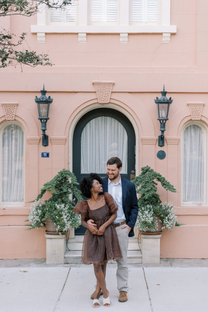 Engaged couple stand together in front of a pink building in Charleston South Carolina