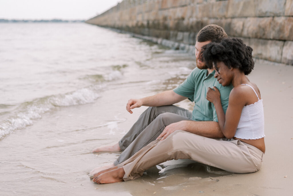 couple sit in the sand and lean on each other