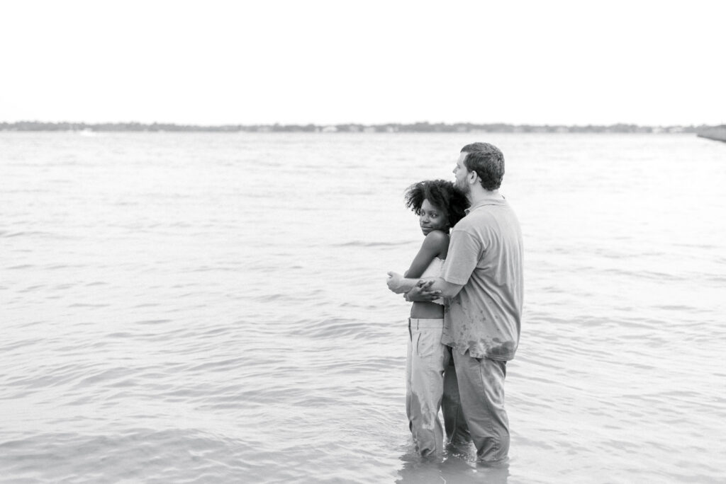 Man hugs his girlfriend from behind standing knee deep in the water