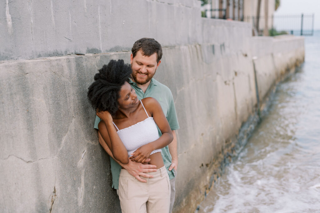 couple hug and lean against a concrete wall 