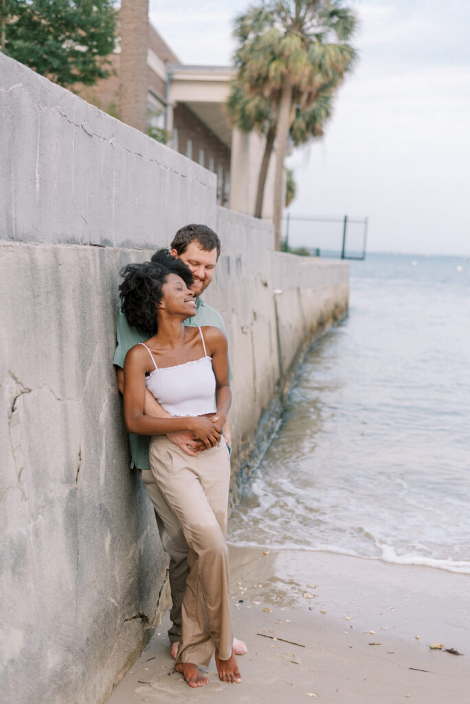 couple lean against each other and stand against the Charleston battery wall