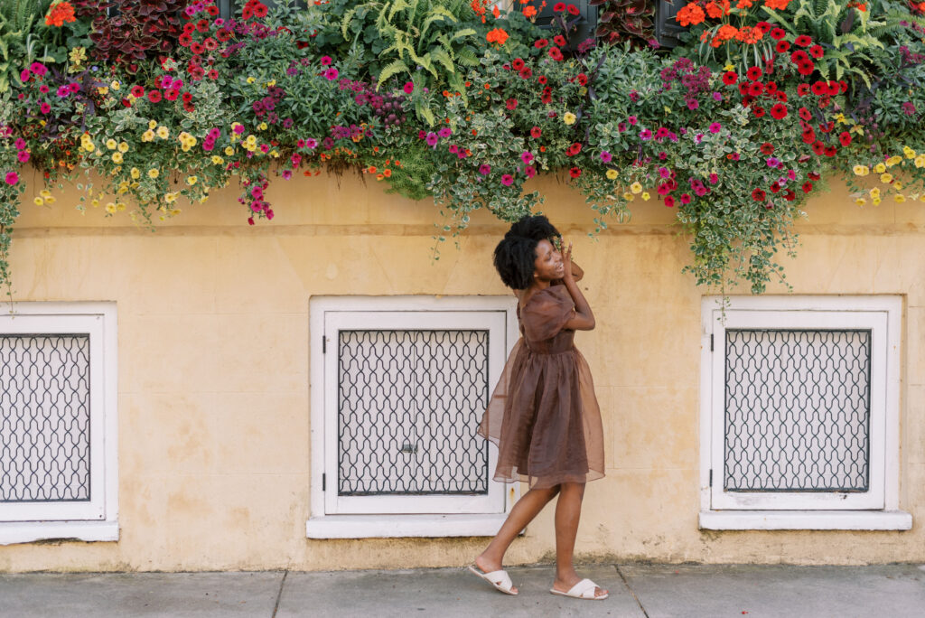 woman in a tulle dress walks in front of a yellow house with overflowing flower boxes in Charleston