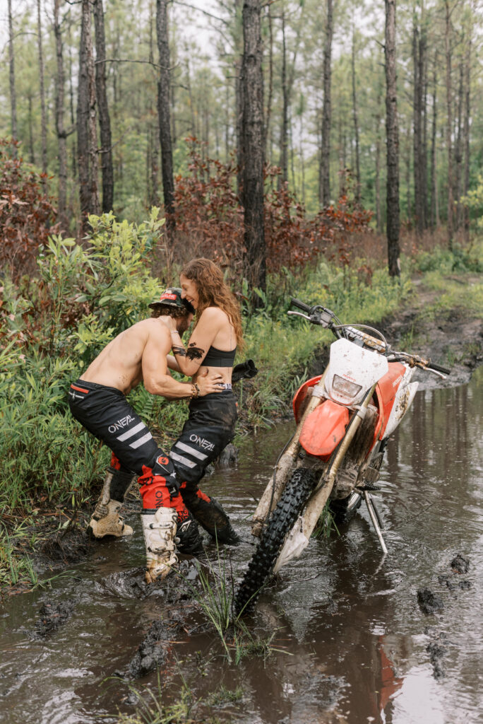 Couple wrestles beside a dirt bike in a mud hole