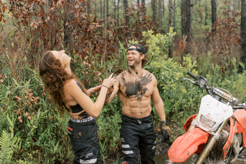 Couple smear mud on each other and have a mud fight laughing during their dirt bike photos