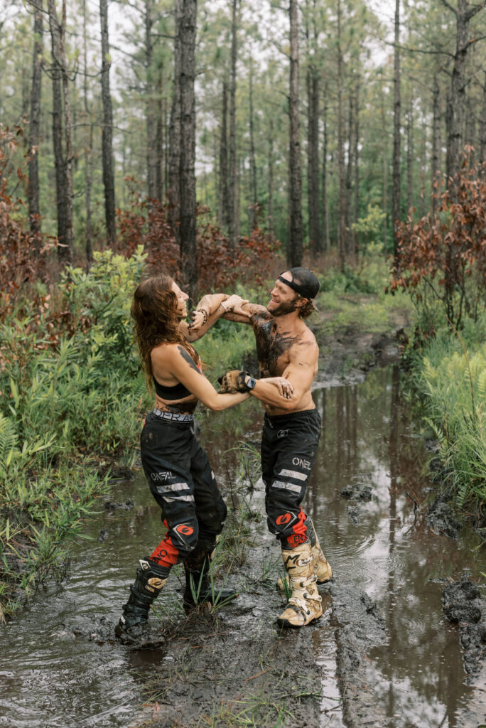 couple covered in mud wrestle in a mud pit during their dirt bike engagement photos