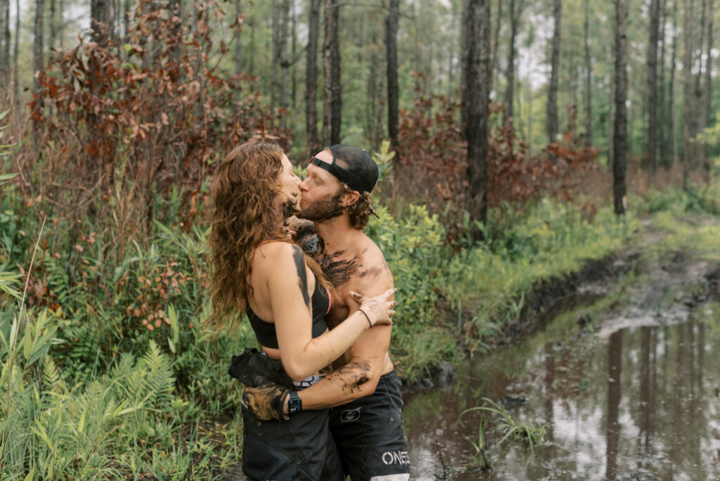 Couple covered in mud kiss in the middle of a mud pit in the woods