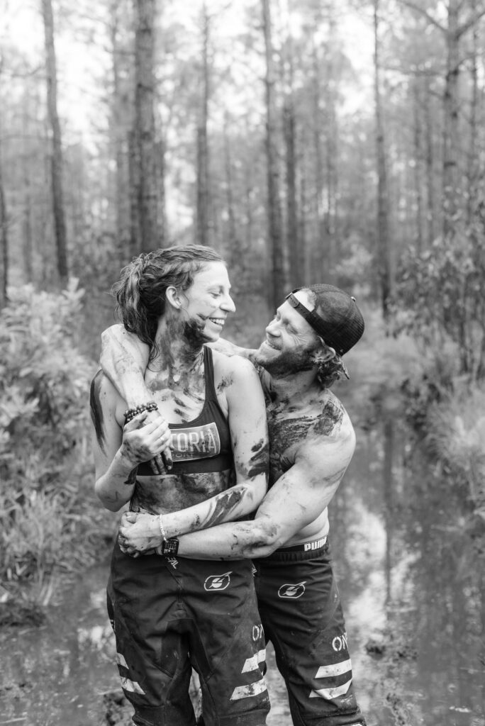 black and white image of a couple hugging covered in mud and smiling at each other