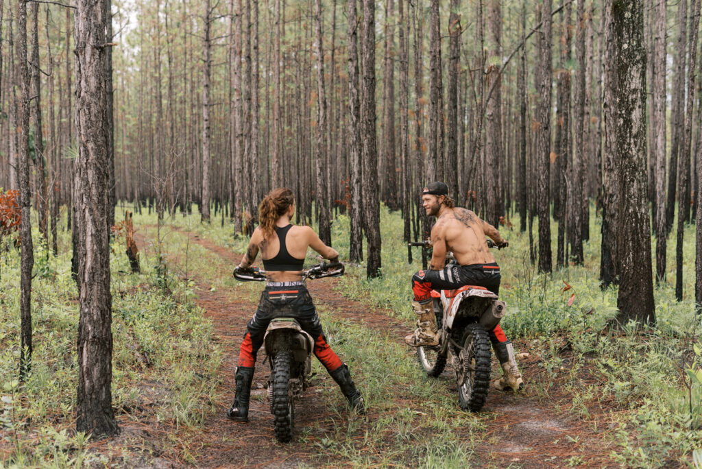 couple on dirt bikes looking into the woods before riding wearing only black and red oneil pants and boots