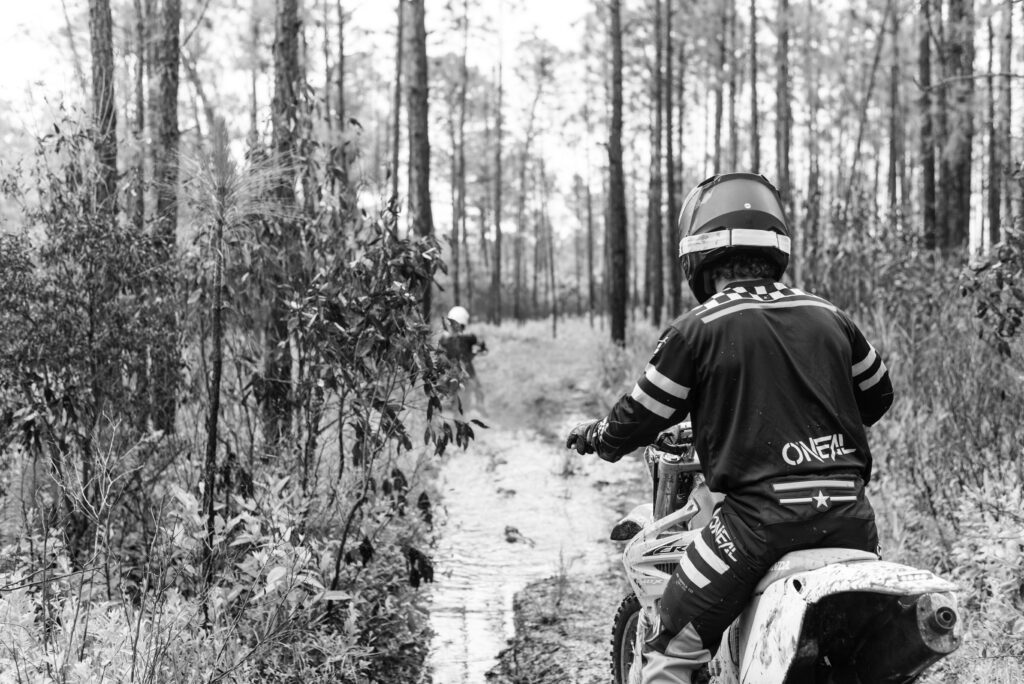 Black and white image of the back of a dirt bike rider looking at a mud pit and sitting on his bike. He's wearing oneil clothes