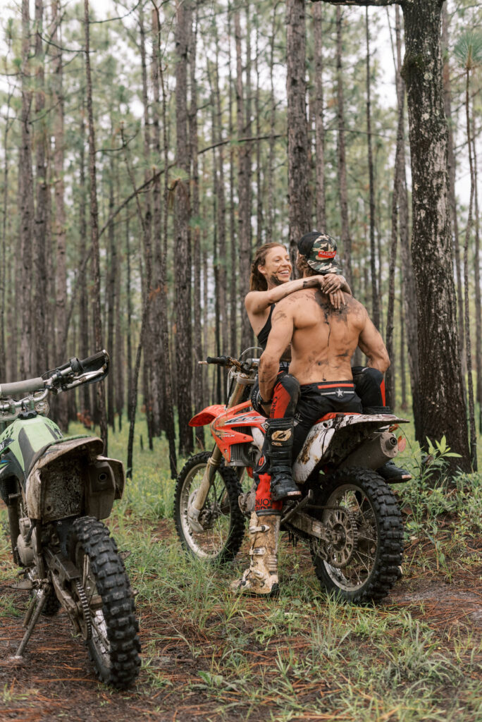 woman sitting on her boyfriend's lap on his bike in the middle of the woods