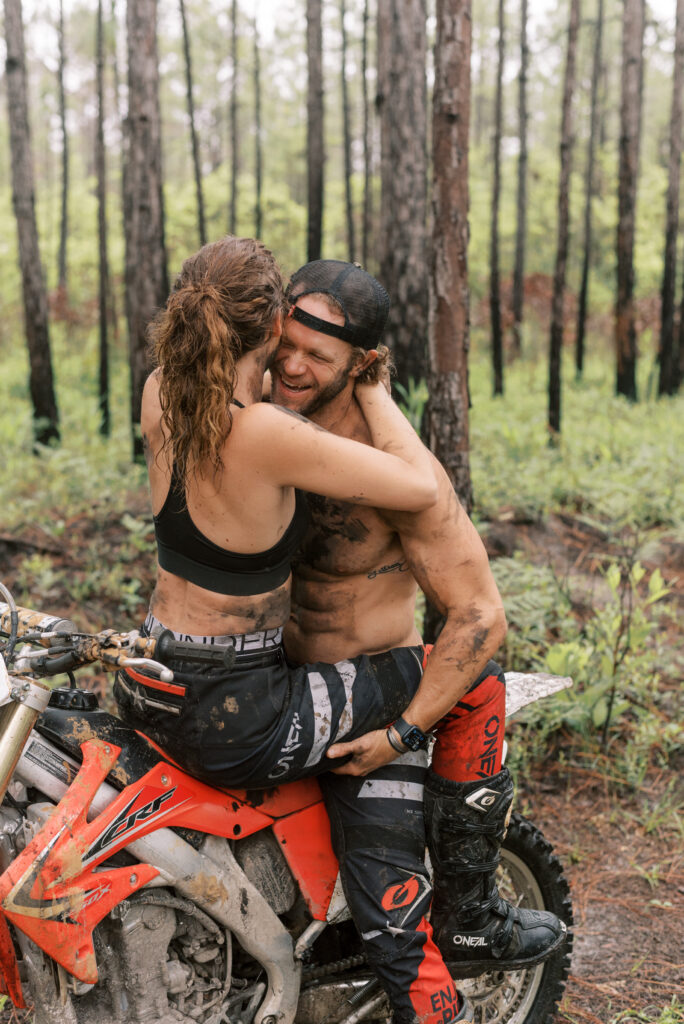 couple laughing together sitting on one dirt bike while boyfriend holds his girlfriend on his lap