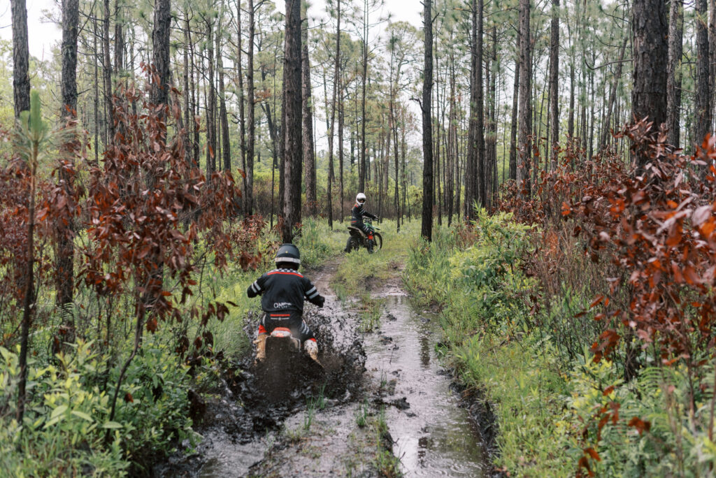 One dirt biker looks back as her boyfriend rides through a deep mud pit on his dirtbike in the South Carolina woods