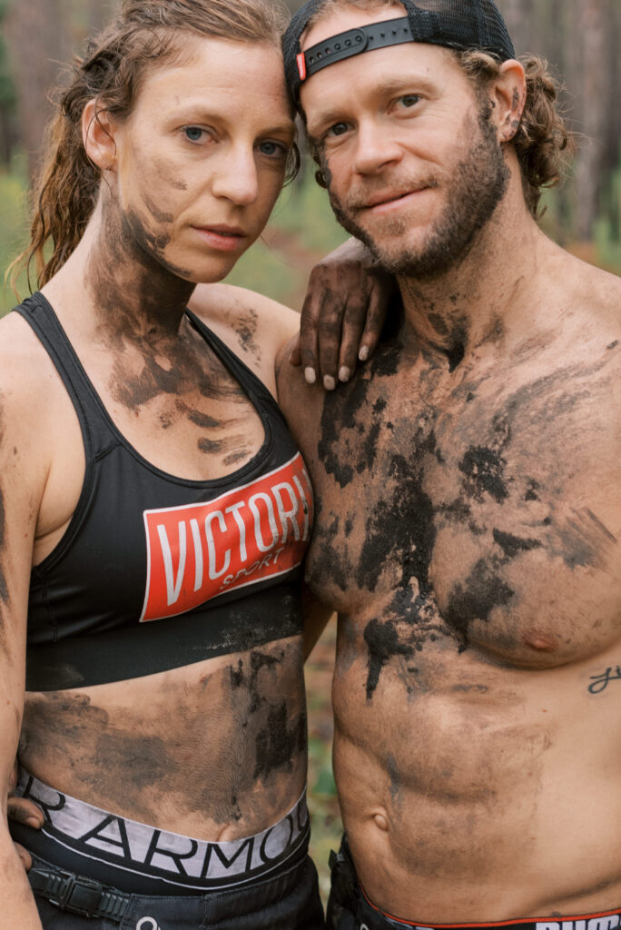 Couple looking at the camera and leaning on each other. Covered in mud