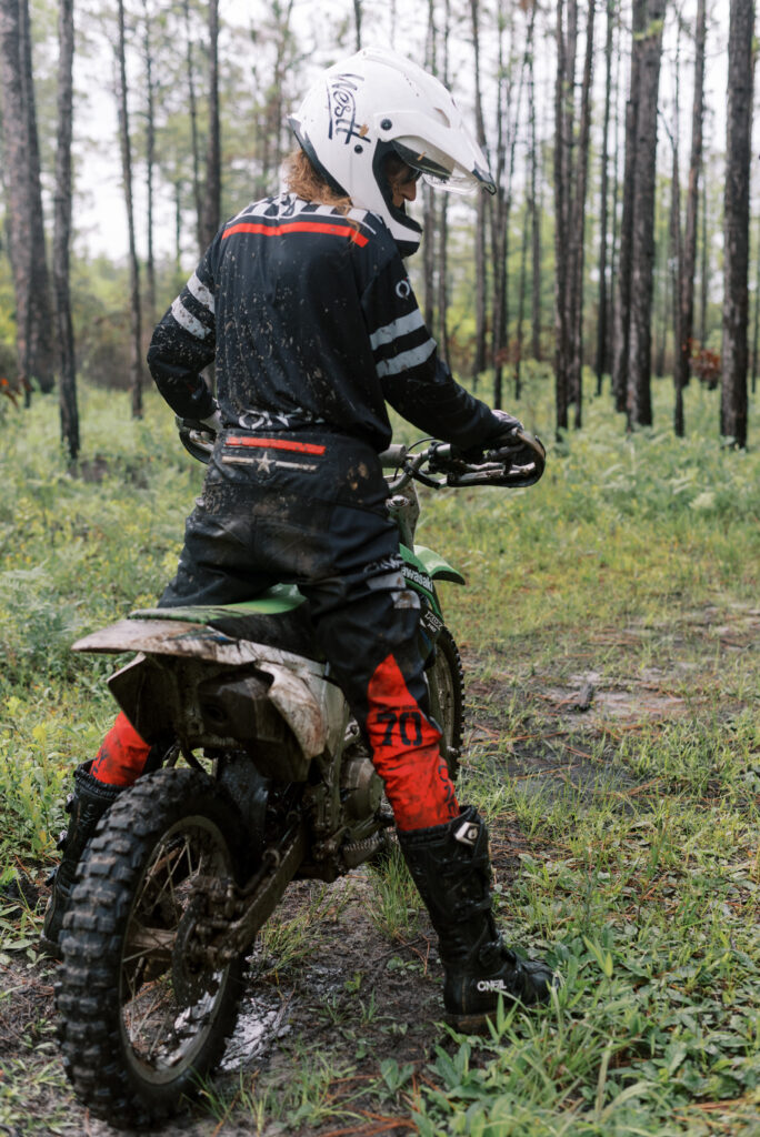 Woman standing on her dirt bike wearing black and red Oneil riding clothes and a white helmet