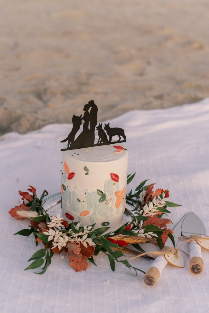 painted wedding cake on a blanket on the beach at sunset