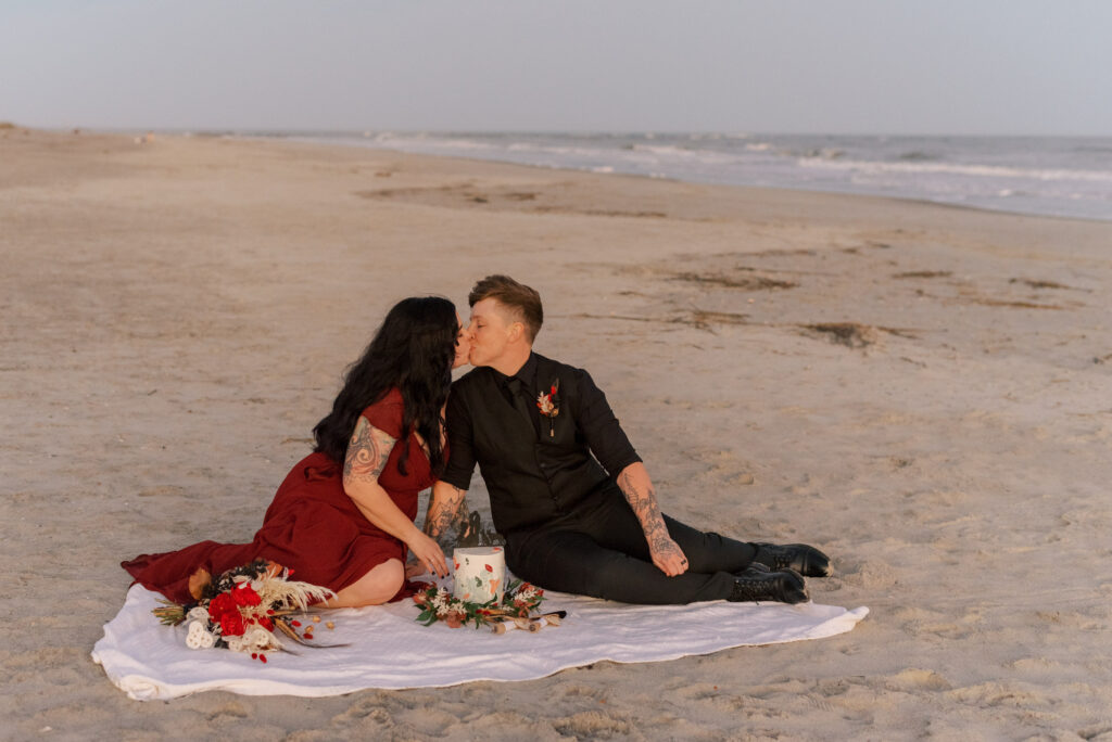 two brides kiss on a blanket before cutting their wedding cake