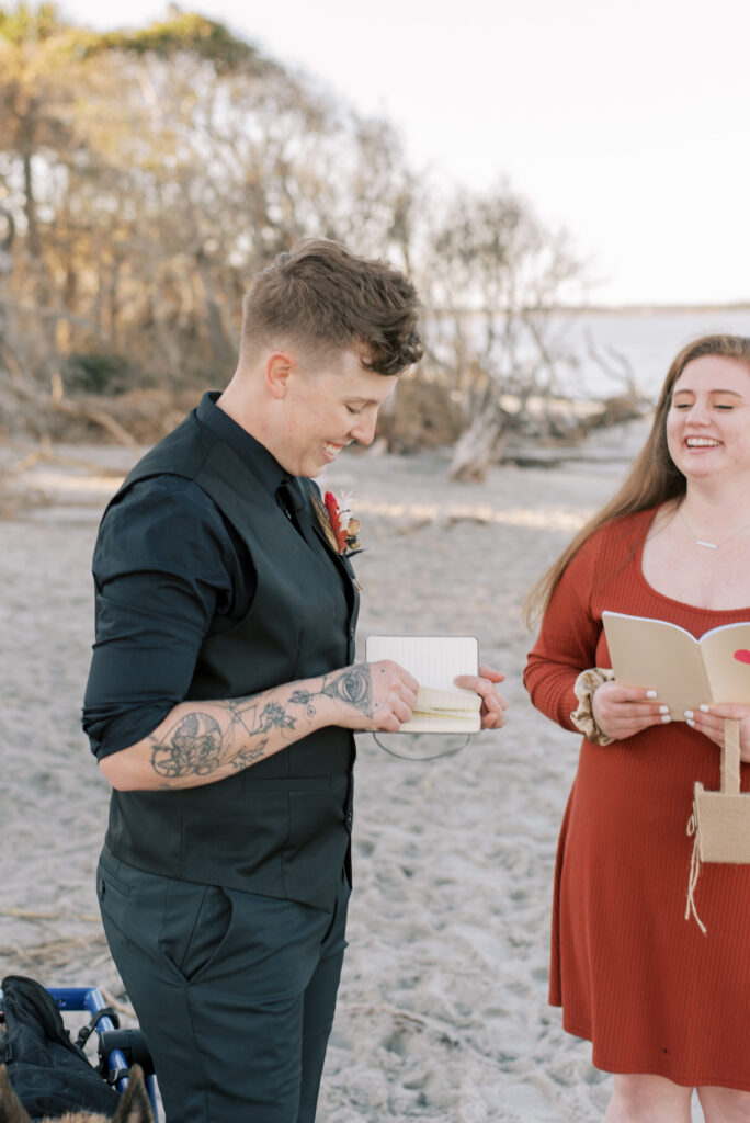 Bride in a black suit reads her vows on the beach at sunset