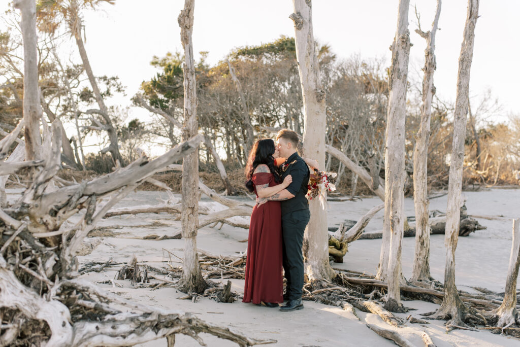 newly married couple kiss in front of driftwood on the beach in South Carolina