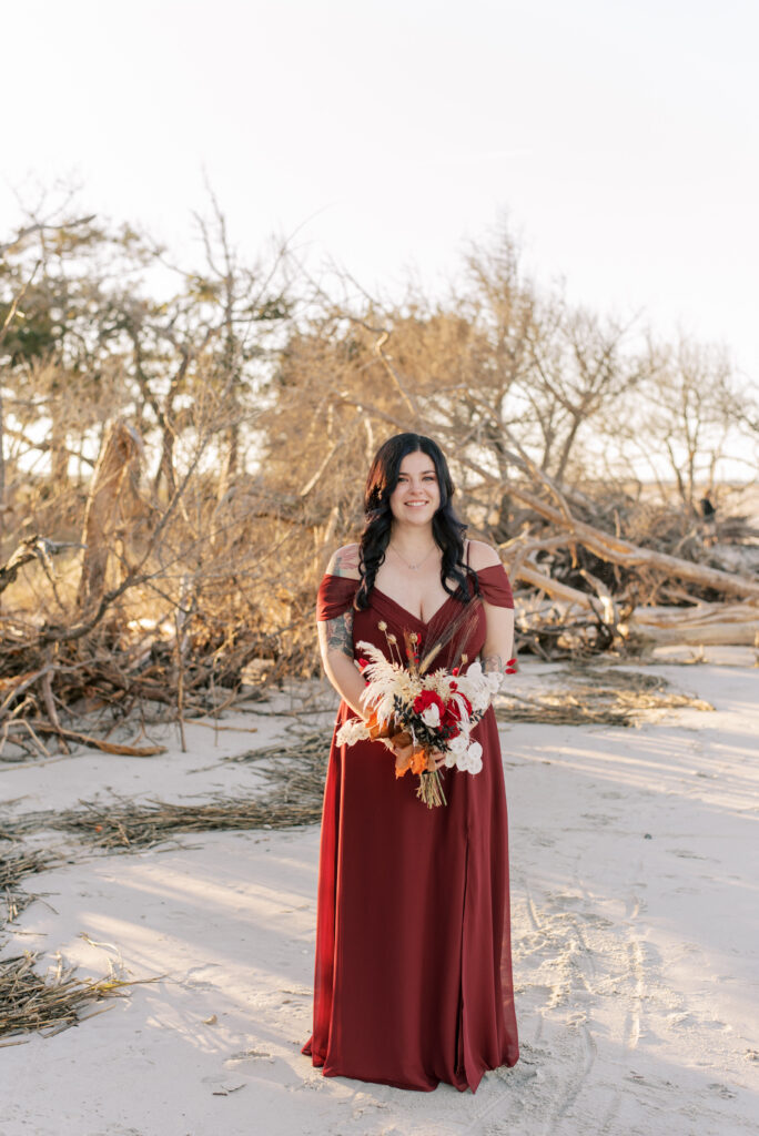 Bride in a burgundy dress on the beach with the sun behind her