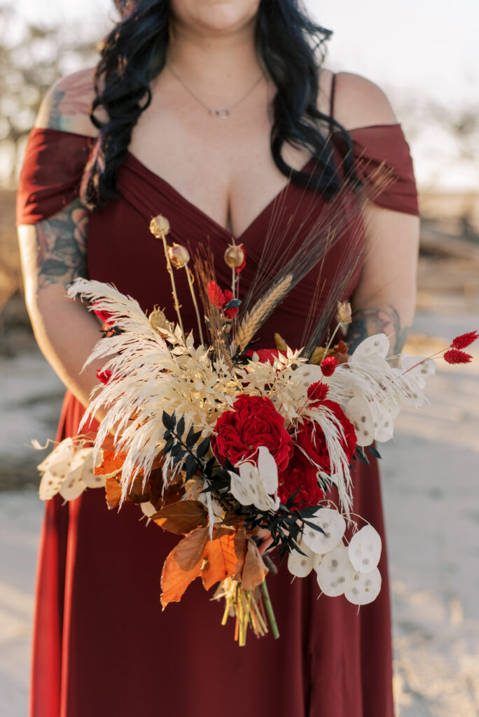 Close up of a bride in a burgundy dress holding her bouquet of dried flowers