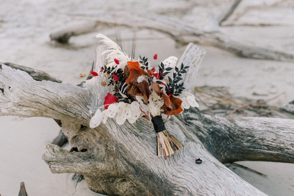 bouquet sits on a piece of driftwood, flowers are white and black and red with dried leaves